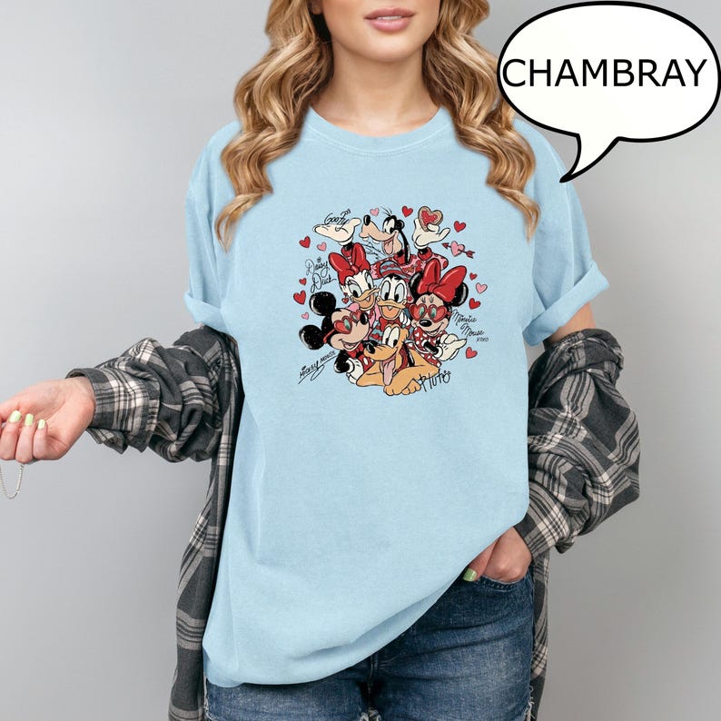 May include: Pale blue t-shirt with a graphic of Disney characters, including Mickey and Minnie Mouse, surrounded by hearts. The word "Chambray" is in a speech bubble. The shirt has rolled-up sleeves.