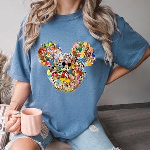 May include: A blue t-shirt with a large Mickey Mouse head design made up of various Disney characters. The design is in a collage style with many different characters from Disney movies and shows.