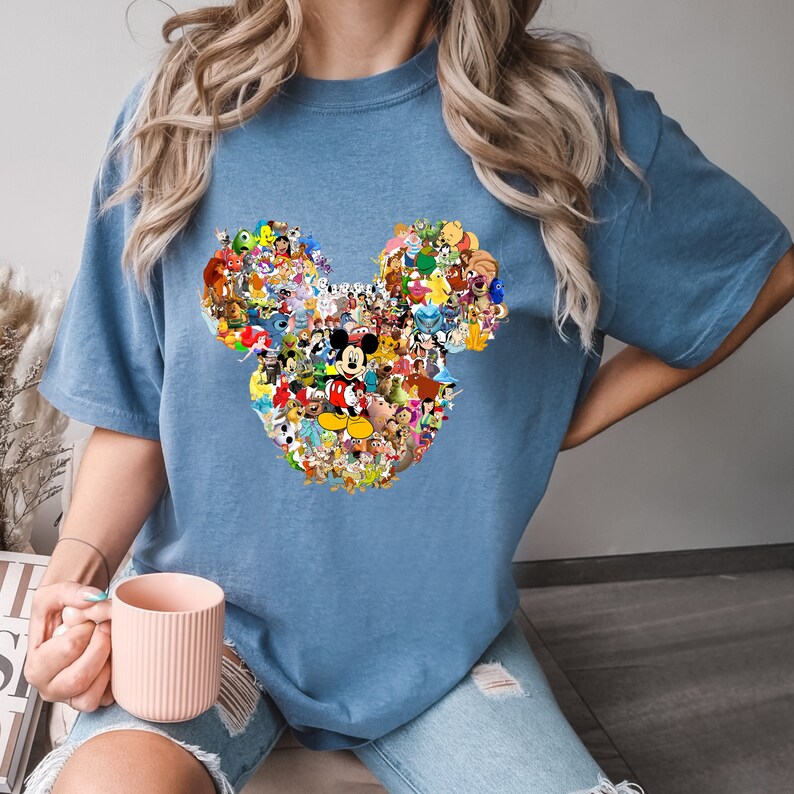 May include: A blue t-shirt with a large Mickey Mouse head design made up of various Disney characters. The design is in a collage style with many different characters from Disney movies and shows.