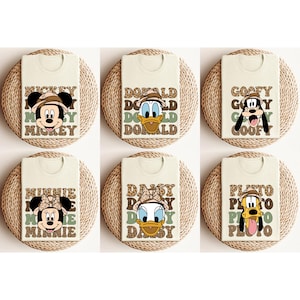 May include: Six white t-shirts featuring different Disney characters and names printed on them. The characters are Mickey Mouse, Minnie Mouse, Donald Duck, Daisy Duck, Goofy, and Pluto. The shirts have a brown and green animal print background.