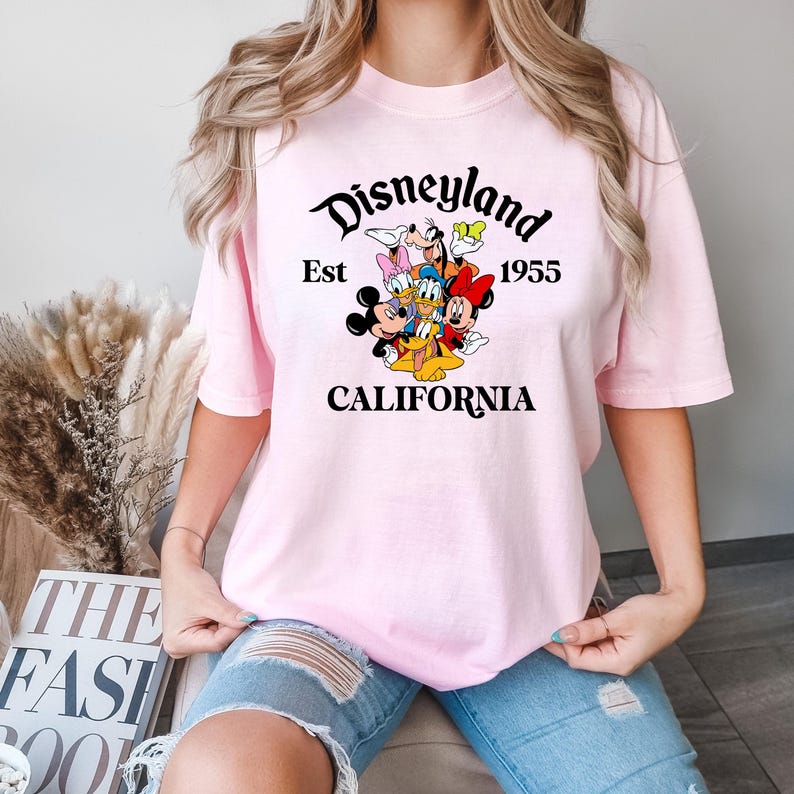 Puede incluir: Camiseta rosa con un gr&aacute;fico negro de Mickey Mouse y sus amigos. El gr&aacute;fico dice "Disneyland Est 1955 California".