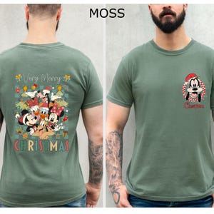 Pode incluir: Camiseta verde musgo com um design de Natal com Mickey Mouse, Minnie Mouse, Pato Donald e Pateta. A parte de tr&aacute;s da camisa tem as palavras "Very Merry Christmas". A frente tem um gr&aacute;fico do Pateta com um chap&eacute;u de Papai Noel.