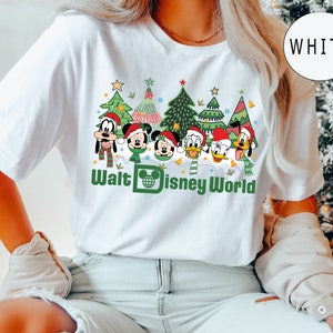 May include: White t-shirt with a Christmas-themed design featuring Mickey Mouse, Minnie Mouse, Goofy, Donald Duck, and Daisy Duck in front of Christmas trees. The text "Walt Disney World" is printed below the characters.
