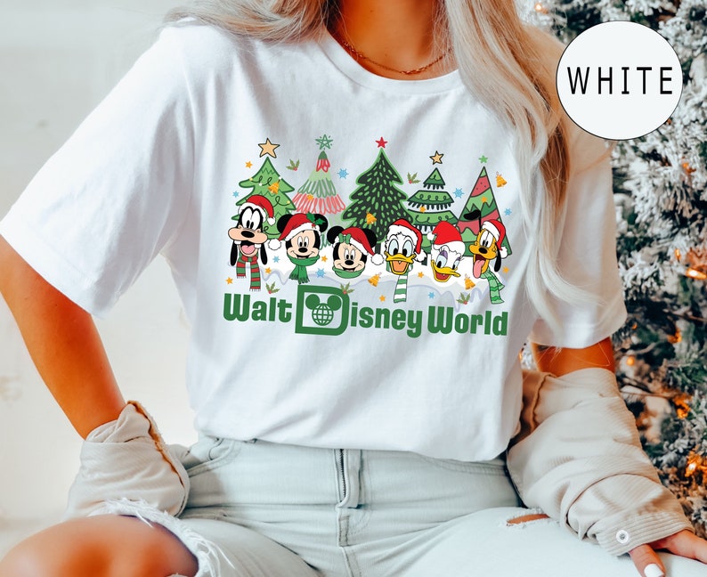 May include: White t-shirt with a Christmas-themed design featuring Mickey Mouse, Minnie Mouse, Goofy, Donald Duck, and Daisy Duck in front of Christmas trees. The text "Walt Disney World" is printed below the characters.