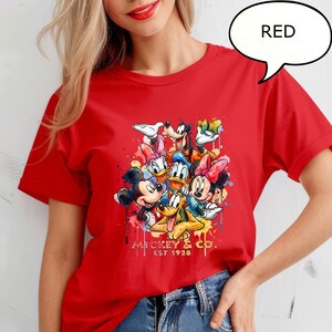 May include: Red t-shirt featuring a colorful graphic of Mickey Mouse, Minnie Mouse, Donald Duck, Daisy Duck, Goofy, and Pluto. The graphic includes the text "Mickey & Co. EST 1928". The shirt is a vibrant red color.