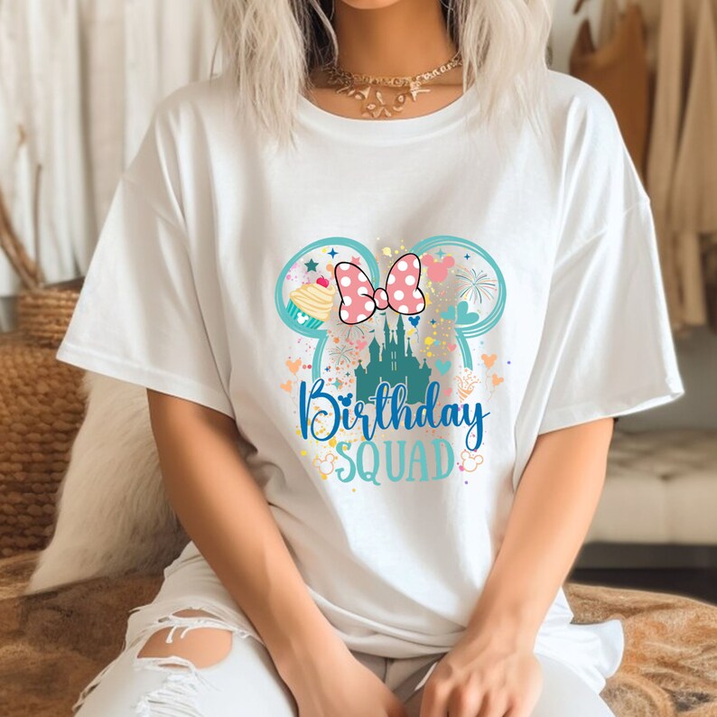 Puede incluir: Camiseta blanca con un gr&aacute;fico colorido de orejas de Mickey Mouse, un castillo, una magdalena y fuegos artificiales. El texto "Birthday Squad" est&aacute; impreso debajo del gr&aacute;fico.
