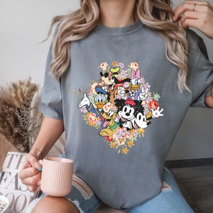 May include: A grey t-shirt featuring a colourful graphic print of Mickey Mouse and his friends surrounded by flowers.