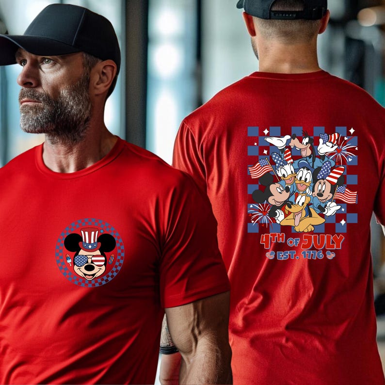 Pode incluir: T-shirts vermelhas com designs patri&oacute;ticos do Mickey Mouse. Uma camisa apresenta Mickey com um chap&eacute;u e &oacute;culos de sol patri&oacute;ticos. A outra camisa tem personagens da Disney com bandeiras e fogos de artif&iacute;cio, com texto "4th of July".