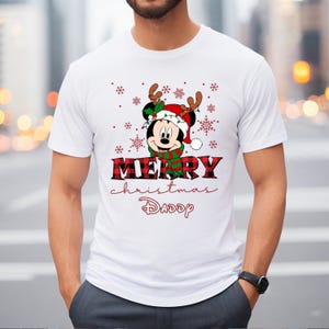 Op de afbeelding: Wit T-shirt met een rood-zwart ruitpatroon. Het ontwerp bevat een cartoon Mickey Mouse met een kerstmanmuts en rendiergewei. De tekst "Merry Christmas Daddy" staat onder de afbeelding.