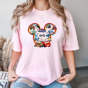 Puede incluir: Camiseta rosa con un dise&ntilde;o de silueta de Mickey Mouse con varios personajes de Cars, incluyendo Rayo McQueen, Mate y Mate el remolcador.