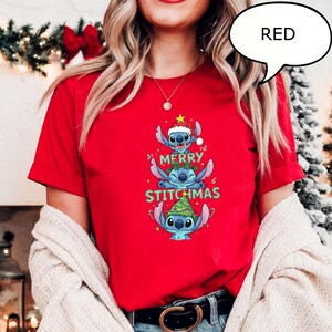 May include: A red t-shirt featuring a stacked design of the character Stitch from the movie Lilo & Stitch, with the text "MERRY STITCHMAS". Stitch is wearing a Santa hat and a Christmas tree. The word "RED" is in a speech bubble.