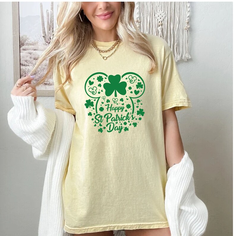 May include: A yellow t-shirt with a green shamrock design in the shape of Mickey Mouse ears. The design includes the text "Happy St. Patrick's Day".