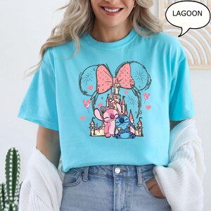 Puede incluir: Una camiseta azul claro con un gr&aacute;fico de dibujos animados de dos personajes, un castillo rosa y un lazo rosa. Los personajes son rosas y azules. La palabra "LAGOON" est&aacute; en un bocadillo en la esquina superior derecha.