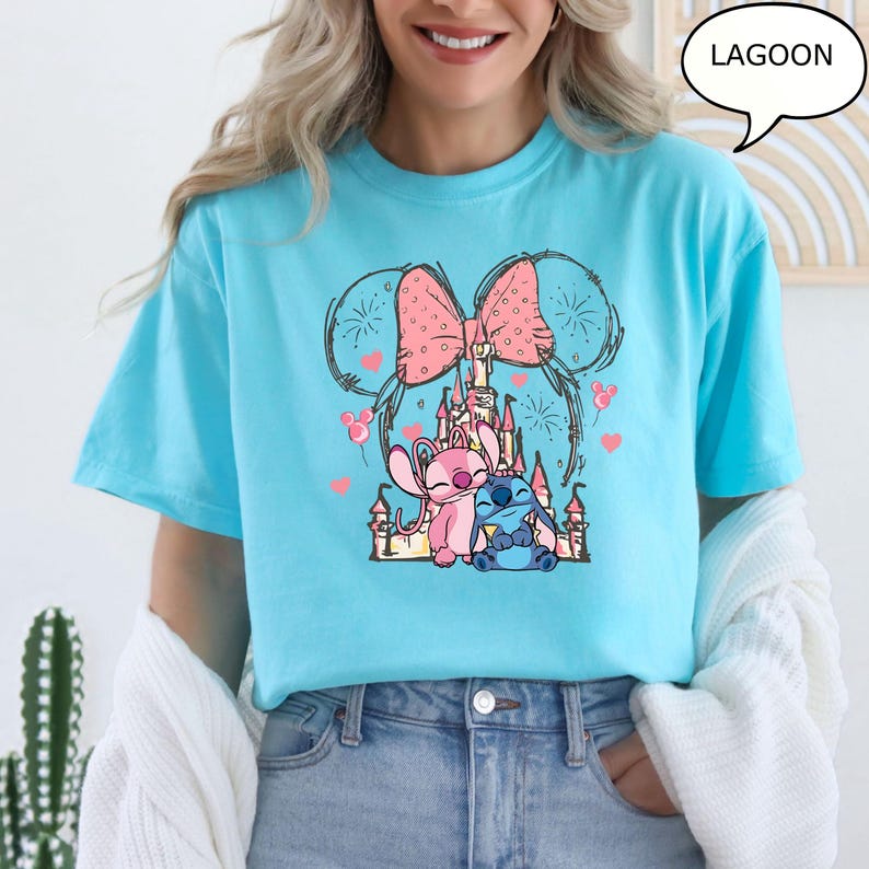 Puede incluir: Una camiseta azul claro con un gr&aacute;fico de dibujos animados de dos personajes, un castillo rosa y un lazo rosa. Los personajes son rosas y azules. La palabra "LAGOON" est&aacute; en un bocadillo en la esquina superior derecha.