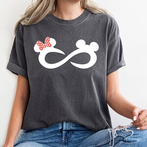 K&ouml;nnte beinhalten: Ein dunkelgraues T-Shirt mit einem wei&szlig;en Unendlichkeits-Symbol-Design. Das Unendlichkeits-Symbol hat auf der einen Seite eine rote Schleife und Ohren und auf der anderen Seite Ohren.