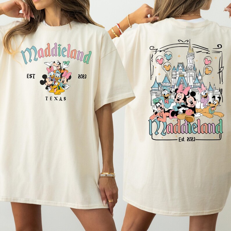 K&ouml;nnte beinhalten: Ein wei&szlig;es T-Shirt mit einem Cartoon-Bild von Mickey Mouse und seinen Freunden auf der Vorderseite. Die R&uuml;ckseite des Shirts zeigt ein Cartoon-Bild von Mickey Mouse und seinen Freunden vor einem Schloss mit dem Text "Maddieland Est. 2023".