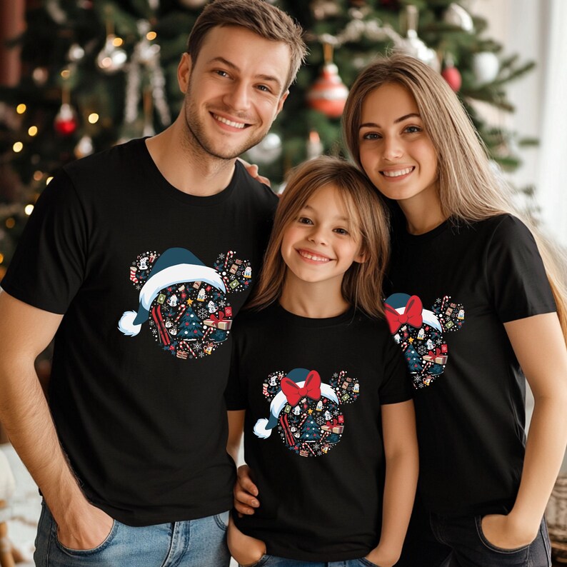 Puede incluir: Tres personas vestidas con camisetas negras a juego con un dise&ntilde;o festivo. El dise&ntilde;o es una cabeza con forma de rat&oacute;n llena de elementos navide&ntilde;os, incluyendo un &aacute;rbol de Navidad, regalos y bastones de caramelo. Las camisetas presentan un gorro de Pap&aacute; Noel o un lazo rojo.