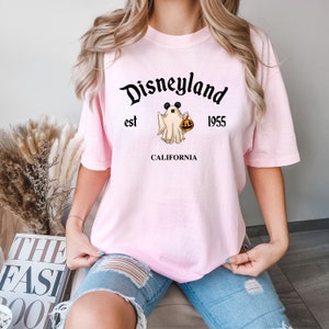 Puede incluir: Camiseta rosa con un gr&aacute;fico negro de un fantasma con orejas de Mickey Mouse y sosteniendo una calabaza. El texto "Disneyland est 1955 CALIFORNIA" est&aacute; impreso en la camiseta.