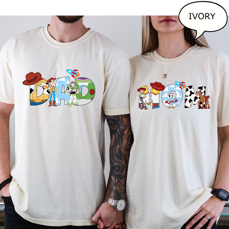 May include: Ivory t-shirts with the words "DAD" and "MOM" in colourful, cartoon-style lettering. The "DAD" shirt features characters and imagery from a popular animated film. The "MOM" shirt has similar design elements.