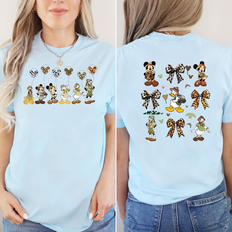 May include: Two light blue t-shirts with a safari animal theme. The front of the shirt features a line of Disney characters holding balloons. The back of the shirt features a pattern of Disney characters, balloons, and bows.