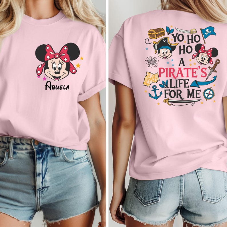 May include: Pink t-shirt featuring a cartoon image of Minnie Mouse on the front with the word "Abuela" underneath. The back of the shirt has a design with Mickey Mouse and Minnie Mouse dressed as pirates with the text "Yo Ho Ho A Pirate's Life For Me".