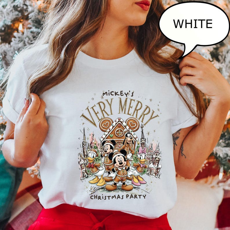 Pu&ograve; includere: T-shirt bianca con grafica festiva. Il design include Topolino, Minnie, Paperino e Pippo davanti a una casa di pan di zenzero. Il testo recita "Mickey's Very Merry Christmas Party".