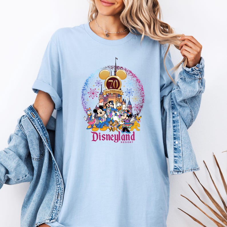 May include: Light blue t-shirt with a graphic of Mickey Mouse and friends celebrating Disneyland's 70th anniversary. The graphic features the Disneyland castle, fireworks, and the text "Disneyland Resort".