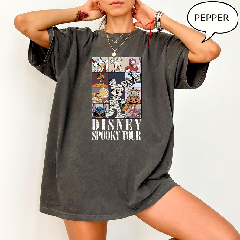 May include: Dark grey t-shirt featuring a colorful graphic of Disney characters in Halloween costumes. The design includes Donald Duck, Mickey Mouse, and Stitch. The text "DISNEY SPOOKY TOUR" is printed below the graphic.