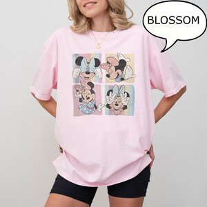 Puede incluir: Una camiseta rosa claro con un gr&aacute;fico de cuatro paneles de Minnie Mouse en varias poses. Cada panel tiene un fondo pastel. La palabra "BLOSSOM" est&aacute; en un bocadillo. La camiseta la lleva una persona.