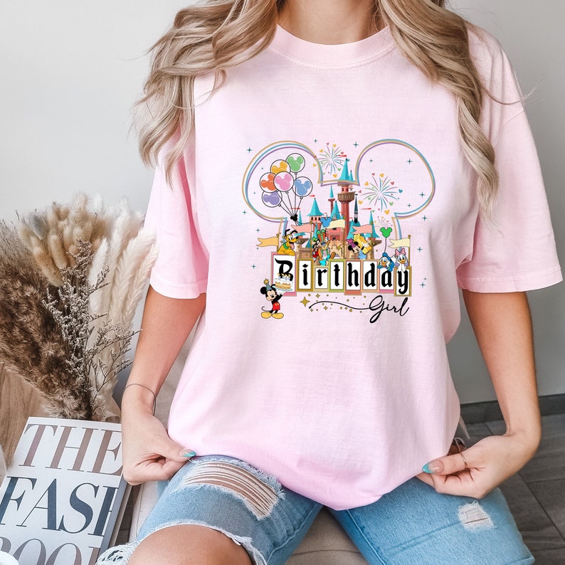 Puede incluir: Camiseta rosa con un gr&aacute;fico de orejas de Mickey Mouse, un castillo, fuegos artificiales y globos. El texto "Birthday Girl" est&aacute; impreso en la camiseta.
