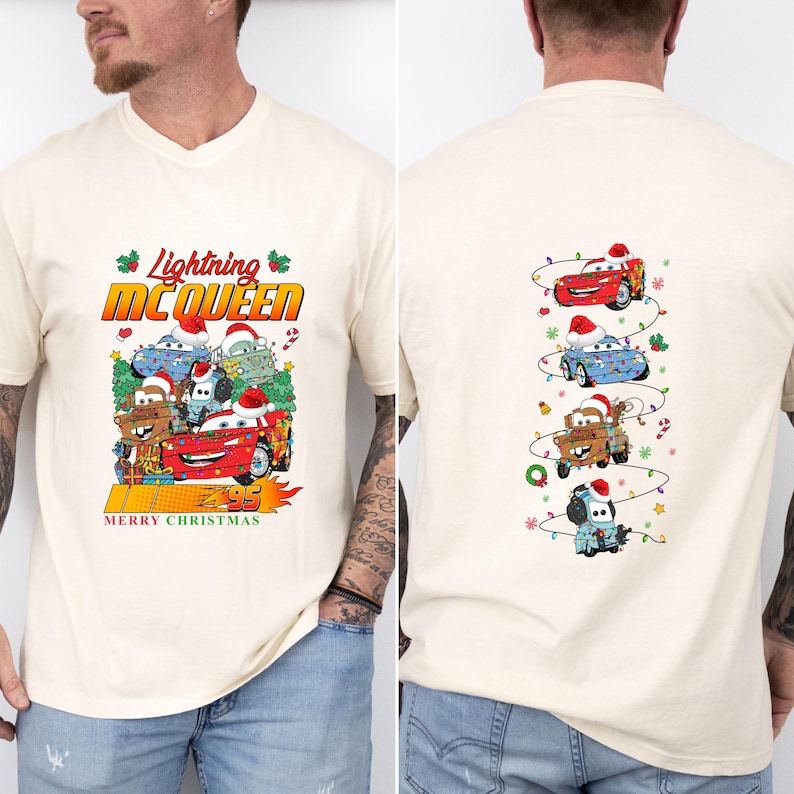 May include: Cream-coloured t-shirt with a Christmas-themed graphic of Lightning McQueen and other Cars characters. The front design includes text that reads "Lightning McQueen" and "Merry Christmas". The back of the shirt shows the Cars characters with Santa hats.