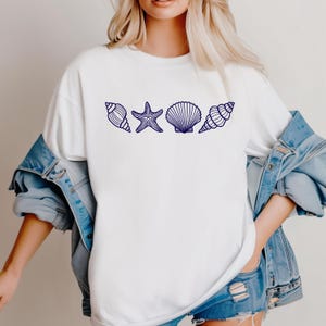 May include: White t-shirt with a navy blue outline of seashells and a starfish.
