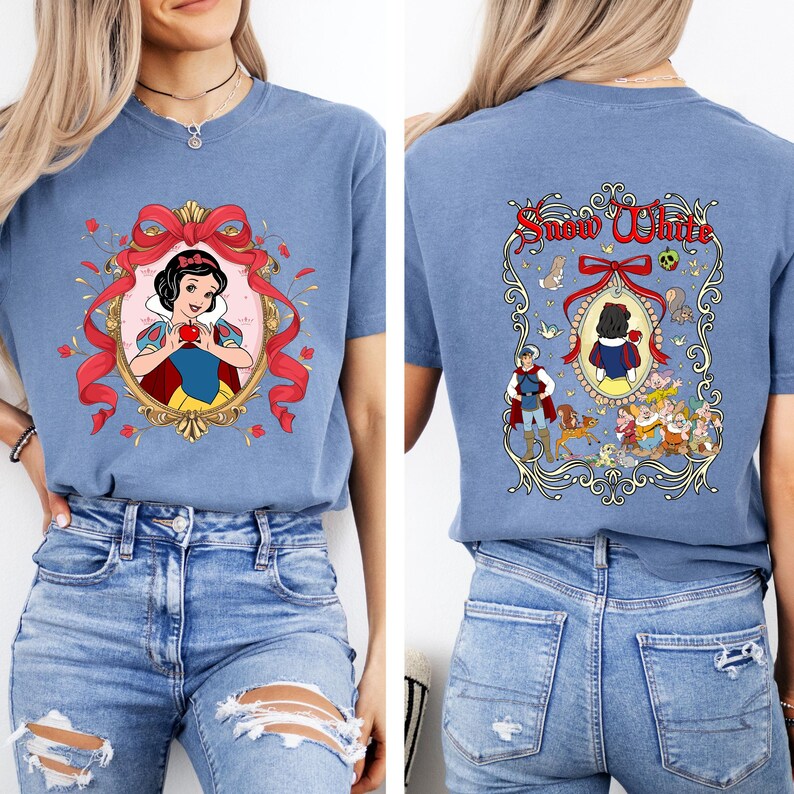 May include: A blue t-shirt featuring a Snow White design. The front graphic shows Snow White holding an apple within a gold frame with a red bow. The back of the shirt has a matching design with the words "Snow White".