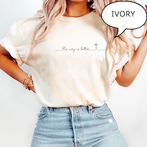 May include: Ivory-colored t-shirt with the text "His way is better" and a cross design. The shirt has a relaxed fit and is made of a soft material. A speech bubble with the word "IVORY" is visible.