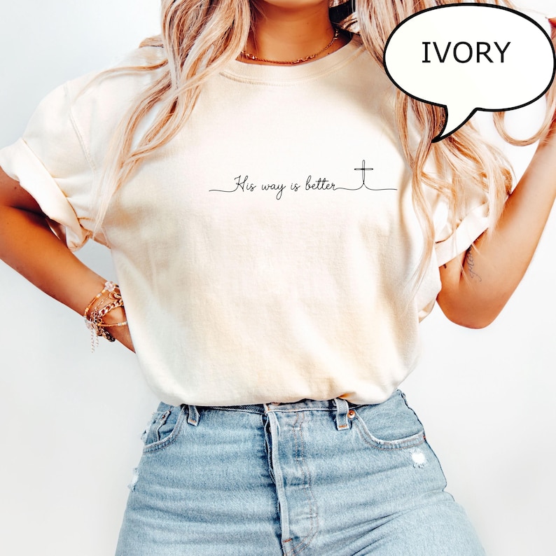 May include: Ivory-colored t-shirt with the text "His way is better" and a cross design. The shirt has a relaxed fit and is made of a soft material. A speech bubble with the word "IVORY" is visible.