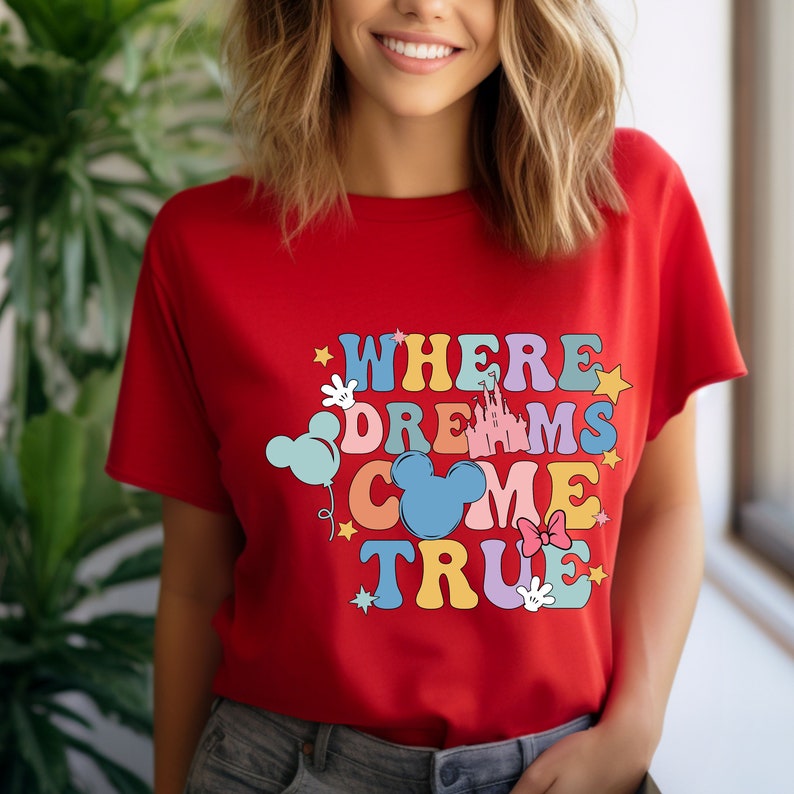 May include: Red t-shirt with a colorful graphic that says "Where Dreams Come True" with Mickey Mouse ears, a castle, stars, and balloons.