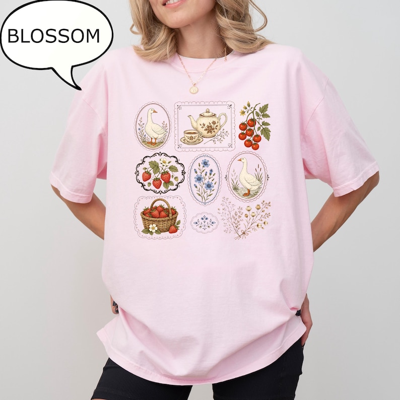 Puede incluir: Una camiseta rosa claro con un estampado gr&aacute;fico de varias ilustraciones enmarcadas que incluyen gansos, una tetera, fresas en una cesta, tomates en rama y ramitas de flores. La palabra BLOSSOM aparece en un globo de texto sobre la camiseta.