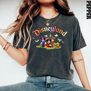 Puede incluir: Una camiseta gris oscuro con un gr&aacute;fico de estilo vintage de Mickey Mouse y sus amigos frente a un cartel de Disneyland. El gr&aacute;fico incluye el texto "Disneyland" en colores arco&iacute;ris.