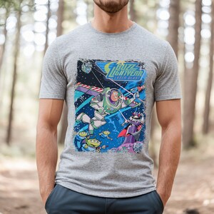 May include: A gray t-shirt with a vintage-style graphic of Buzz Lightyear from the Toy Story franchise. The graphic features Buzz flying in space with a laser blast, along with other characters from the movie. The text "Buzz Lightyear Laser Blast" is printed on the graphic.
