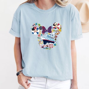 Pu&ograve; includere: T-shirt azzurra con un design a forma di testa di Topolino riempito di elementi nautici. Il design include una nave da crociera, Minnie Mouse e altri personaggi. L'anno "2024" &egrave; incluso.
