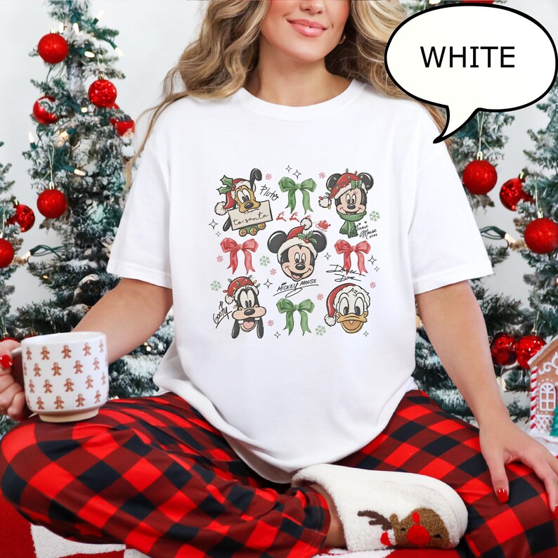 Puede incluir: Camiseta blanca con personajes de Disney con tem&aacute;tica navide&ntilde;a, incluyendo Mickey Mouse, Donald Duck y Goofy, con gorros de Pap&aacute; Noel y lazos. La camiseta tiene la palabra "WHITE" en un bocadillo. Los personajes est&aacute;n rodeados de copos de nieve.