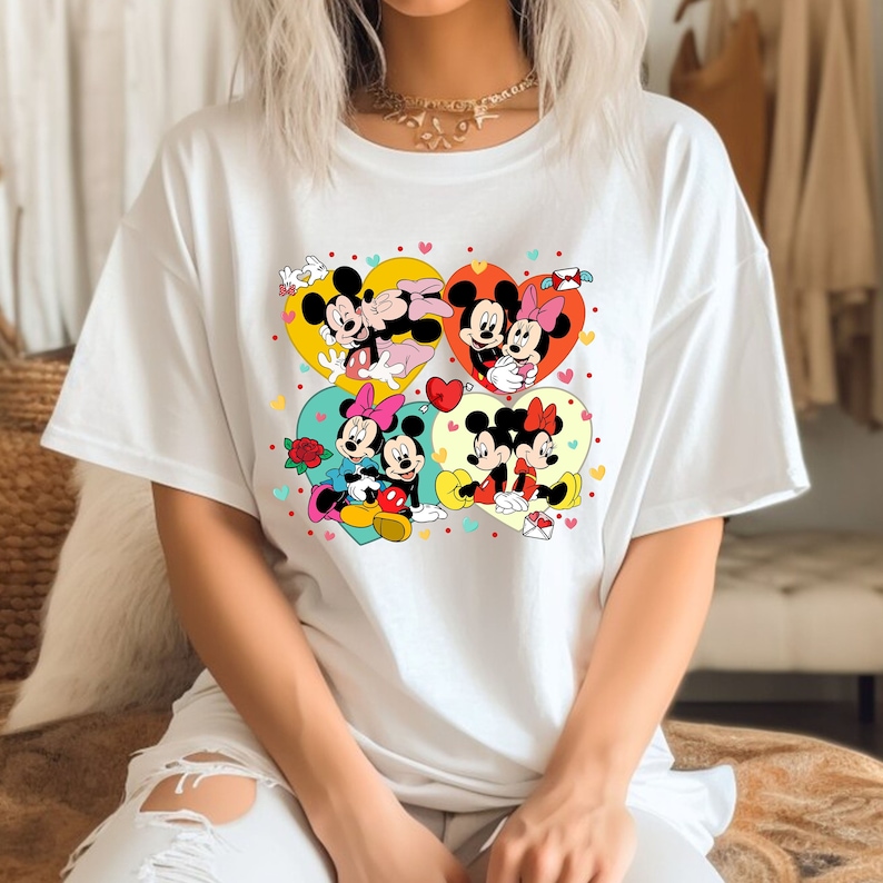 Puede incluir: Camiseta blanca con un estampado gr&aacute;fico colorido de Mickey Mouse y Minnie Mouse en varias poses. El gr&aacute;fico presenta corazones, flores y otros detalles rom&aacute;nticos.