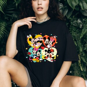 Puede incluir: Camiseta negra con un estampado gr&aacute;fico colorido de Mickey Mouse y Minnie Mouse en cuatro marcos en forma de coraz&oacute;n diferentes. Los corazones est&aacute;n decorados con peque&ntilde;os corazones y flores.