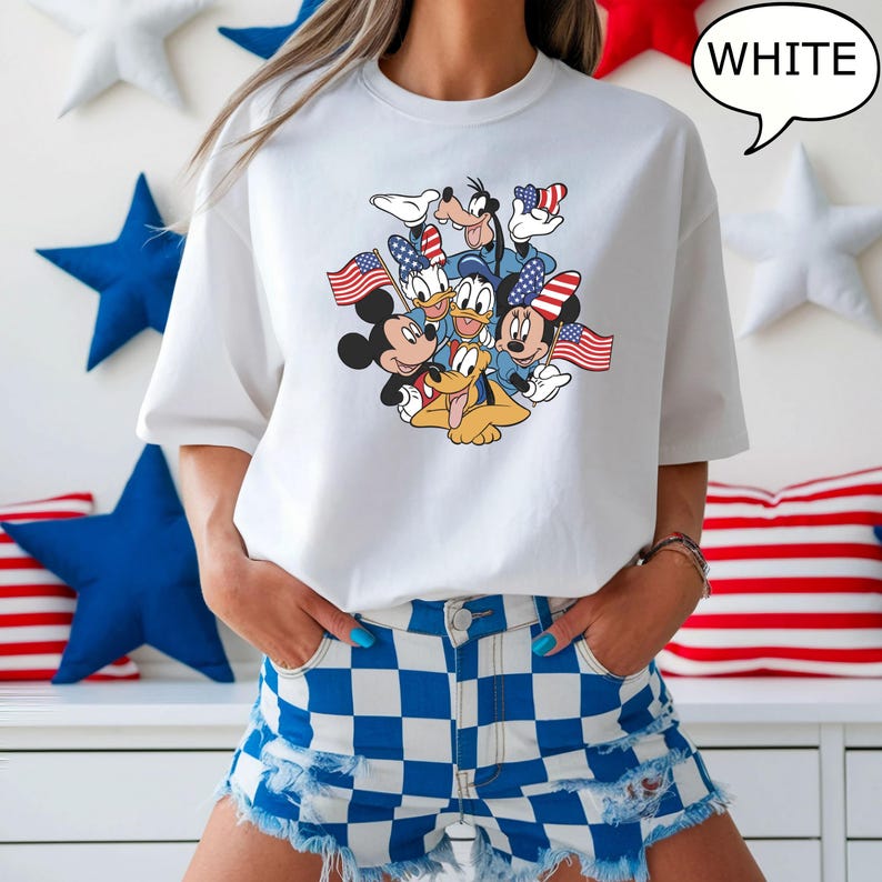 May include: White t-shirt featuring a graphic of Mickey Mouse, Donald Duck, Goofy, and Pluto, each holding American flags or wearing patriotic accessories. The word "WHITE" is in a speech bubble. The shirt is paired with blue and white checkered shorts.