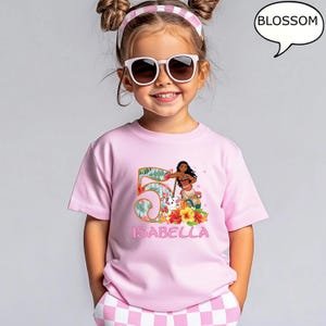 May include: A pink t-shirt featuring a colorful graphic of the number 5 with tropical leaves, a cartoon character, and the name "ISABELLA". The shirt is worn by a young girl wearing sunglasses and a pink and white headband.