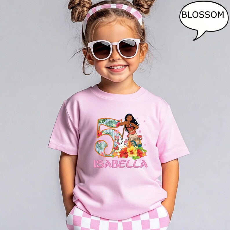 May include: A pink t-shirt featuring a colorful graphic of the number 5 with tropical leaves, a cartoon character, and the name "ISABELLA". The shirt is worn by a young girl wearing sunglasses and a pink and white headband.