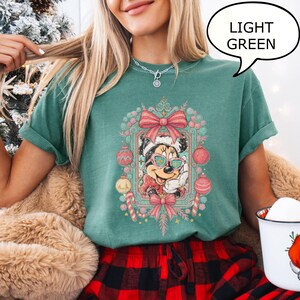 Puede incluir: Camiseta verde claro con un dise&ntilde;o de Minnie Mouse navide&ntilde;a. El dise&ntilde;o incluye gafas de sol, un gorro de Pap&aacute; Noel y adornos festivos. La camiseta tiene las mangas dobladas. Un bocadillo dice "LIGHT GREEN".