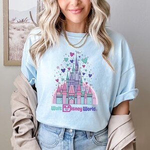 May include: A light blue t-shirt with a graphic of Cinderella's castle with pink, purple, and green balloons and the text "Walt Disney World".