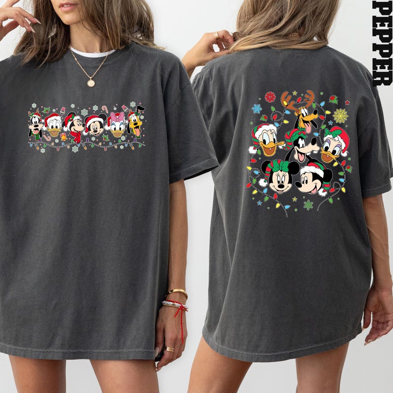 May include: Dark gray t-shirt featuring a festive design with Disney characters wearing Santa hats and surrounded by Christmas lights. The back of the shirt also has a similar design. The shirt is a comfortable, oversized fit.