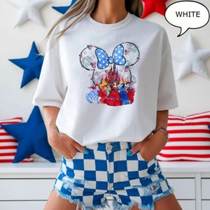 Puede incluir: Camiseta blanca con un dise&ntilde;o de Minnie Mouse con un lazo azul y un castillo. El dise&ntilde;o incorpora elementos de la bandera estadounidense y princesas de Disney. La palabra "WHITE" est&aacute; en una burbuja.
